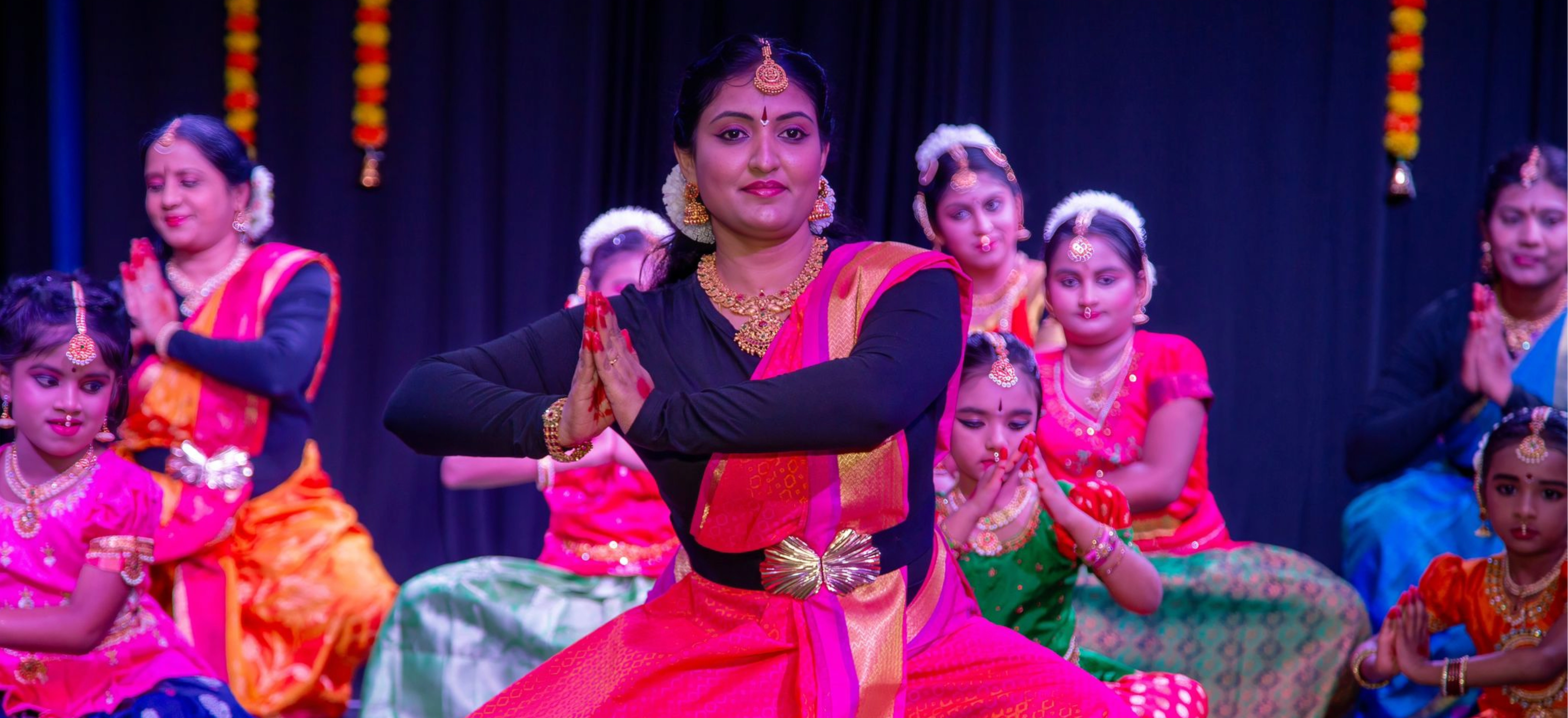 A troupe of Bharatanatyam dancers performing on stage in vibrant costumes